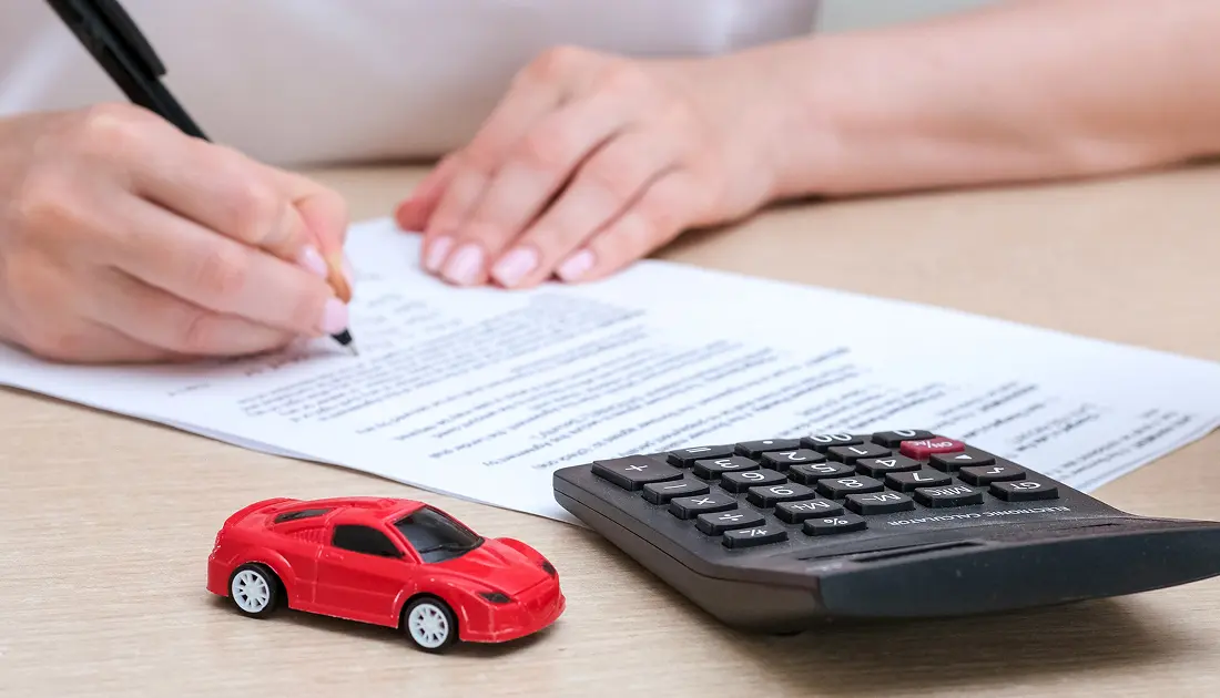 Person signing papers with calculator and car
