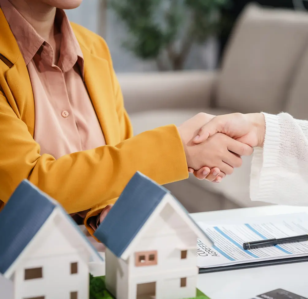 Handshake over real estate documents and model houses